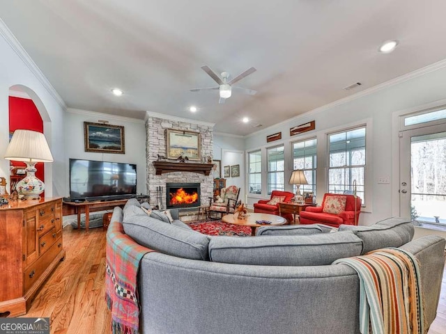 living room featuring recessed lighting, light wood-style flooring, ornamental molding, and a stone fireplace