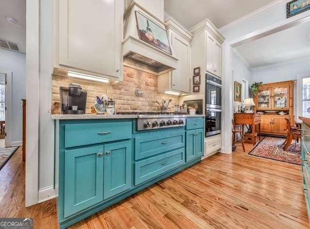 kitchen featuring ornamental molding, custom range hood, light wood-style floors, and blue cabinetry