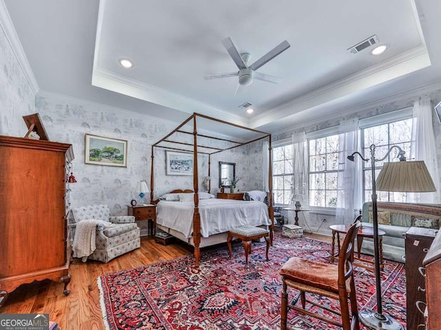 bedroom featuring wood finished floors, a raised ceiling, visible vents, and wallpapered walls