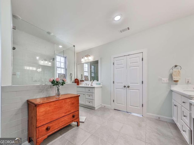 full bath featuring tile patterned floors, visible vents, two vanities, and tiled shower