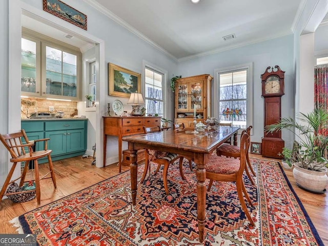 dining area with light wood-type flooring, visible vents, and crown molding