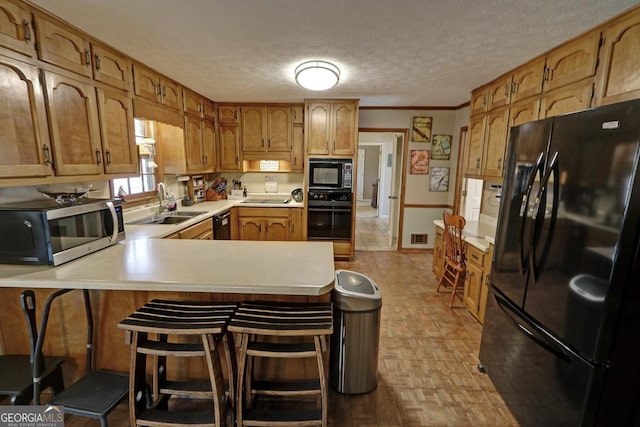 kitchen featuring light countertops, a sink, a textured ceiling, a peninsula, and black appliances