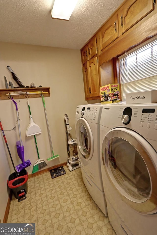 washroom featuring a textured ceiling, baseboards, cabinet space, light floors, and washer and clothes dryer