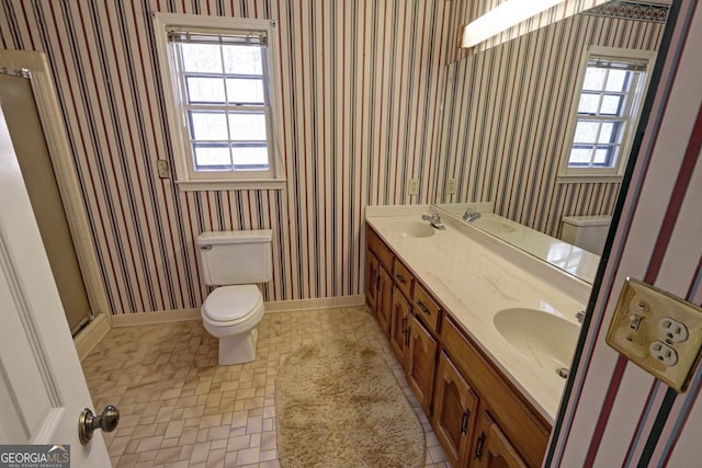 bathroom with toilet, wallpapered walls, and a sink