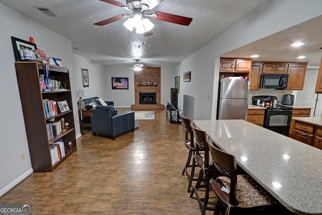 kitchen with a textured ceiling, dark wood-type flooring, visible vents, black appliances, and brown cabinetry