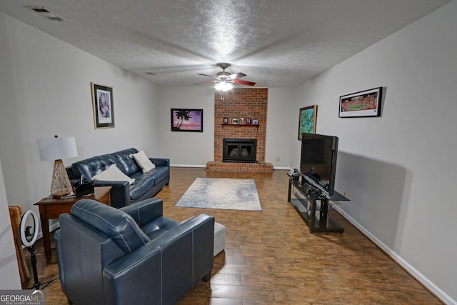 living area with visible vents, a ceiling fan, a brick fireplace, a textured ceiling, and wood finished floors