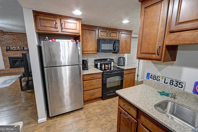 kitchen with light wood-type flooring, black appliances, brown cabinets, and a sink