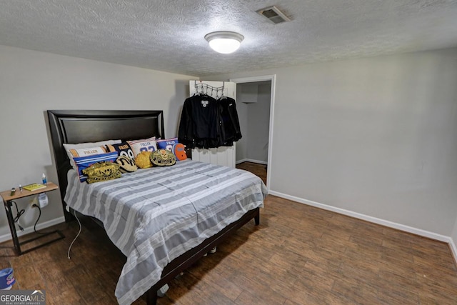 bedroom with visible vents, a textured ceiling, baseboards, and wood finished floors