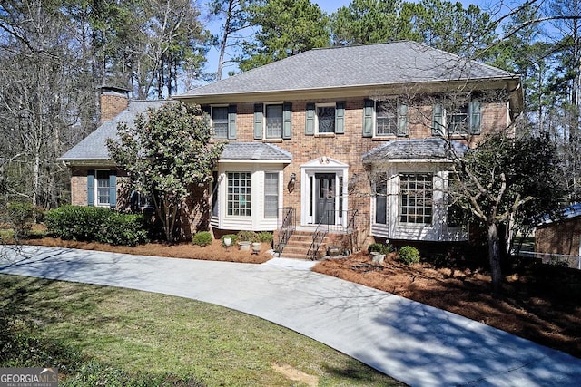 view of front of property with brick siding, a chimney, and roof with shingles