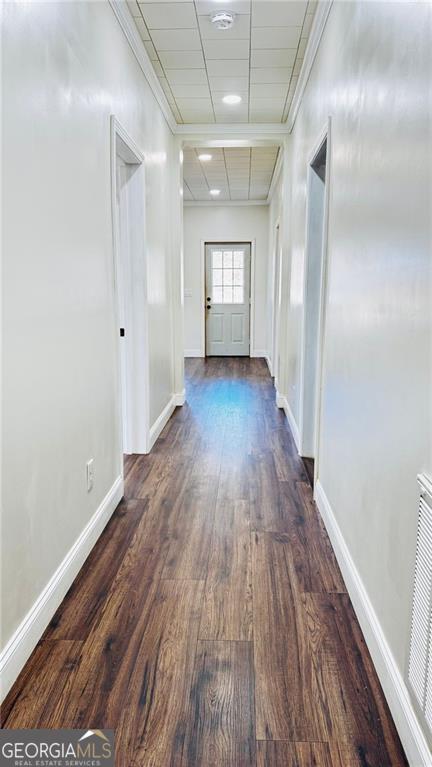 hall featuring crown molding, dark wood finished floors, a paneled ceiling, visible vents, and baseboards