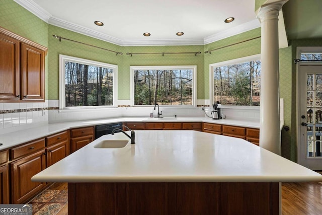 kitchen with a center island with sink, crown molding, light countertops, and a sink