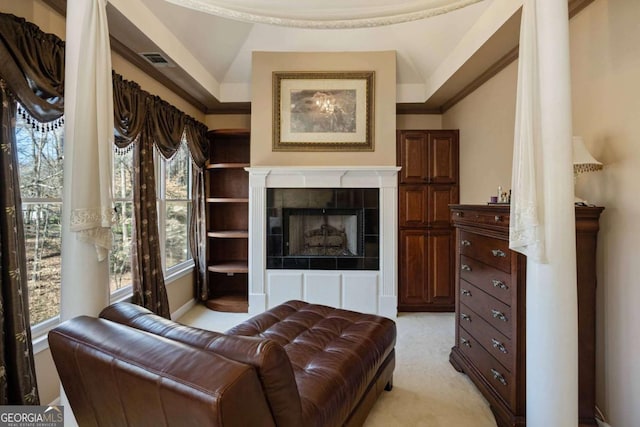 living area featuring a fireplace, light colored carpet, visible vents, and ornamental molding