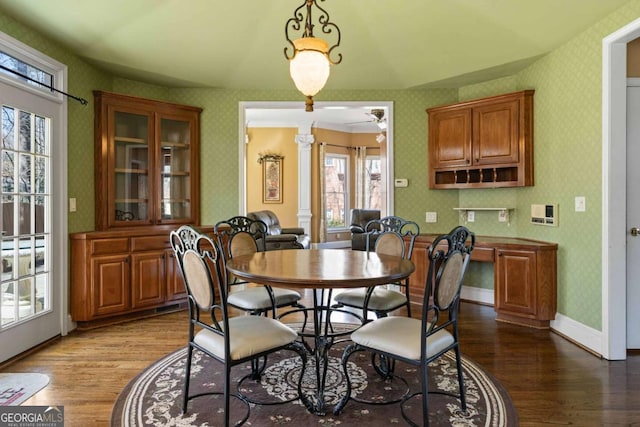 dining area with wood finished floors, wallpapered walls, baseboards, and decorative columns