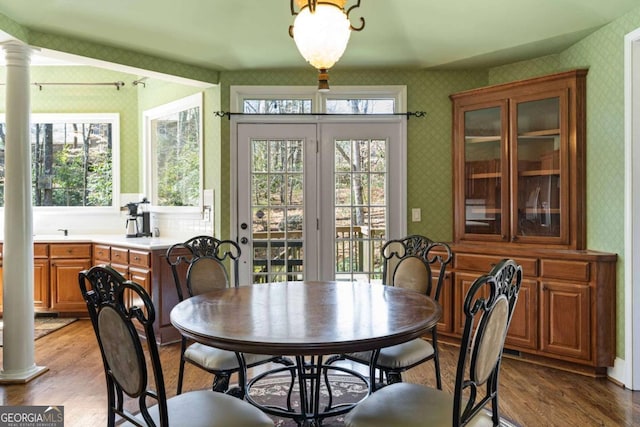 dining area featuring light wood-type flooring, decorative columns, and wallpapered walls