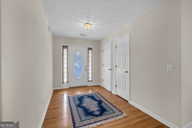 foyer featuring a textured ceiling, wood finished floors, visible vents, and baseboards