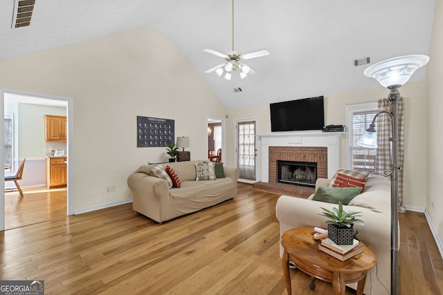 living room featuring light wood finished floors, plenty of natural light, visible vents, and high vaulted ceiling