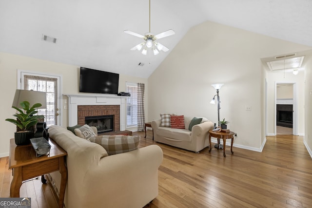 living area with high vaulted ceiling, a brick fireplace, attic access, and light wood-style floors