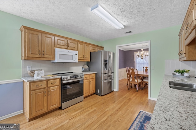 kitchen with visible vents, a wainscoted wall, light wood-style flooring, appliances with stainless steel finishes, and a notable chandelier