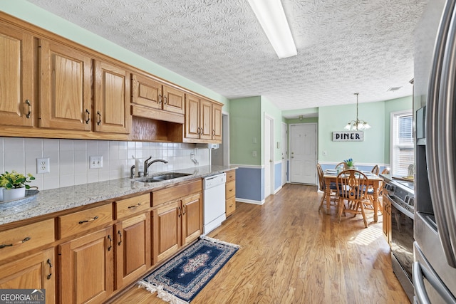 kitchen featuring decorative backsplash, appliances with stainless steel finishes, light wood-style floors, a sink, and light stone countertops