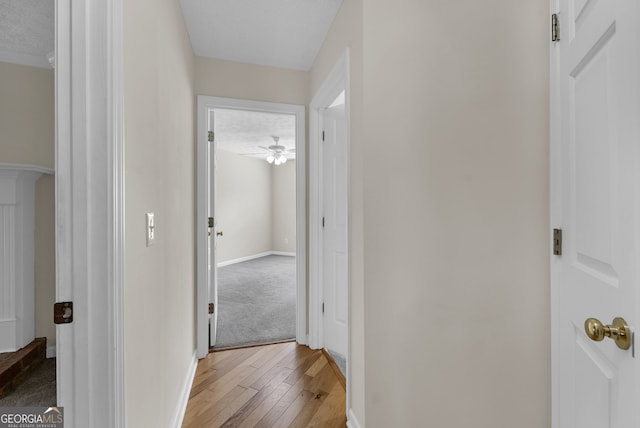 hallway featuring light wood-style flooring, baseboards, and a textured ceiling