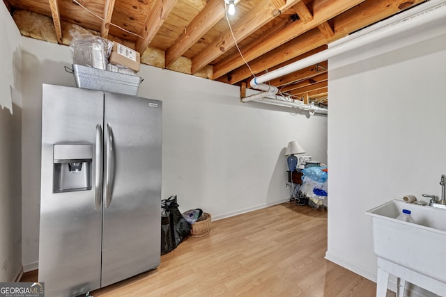 basement with a sink, baseboards, stainless steel refrigerator with ice dispenser, and wood finished floors