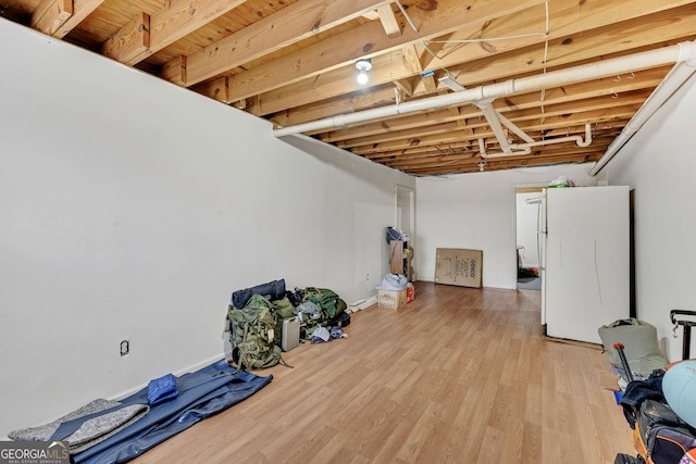 unfinished basement with light wood finished floors and freestanding refrigerator