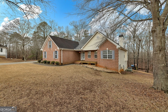 view of front of property featuring a chimney, a front lawn, central AC, and brick siding