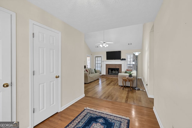 living area featuring lofted ceiling, ceiling fan, a textured ceiling, a fireplace, and wood finished floors