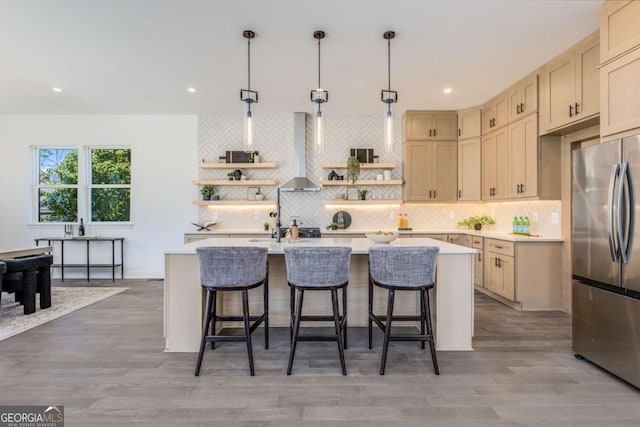 kitchen featuring a breakfast bar, light countertops, wall chimney range hood, freestanding refrigerator, and open shelves