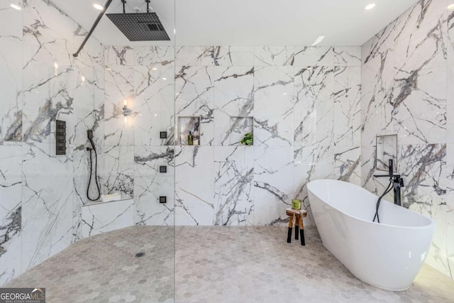 full bath featuring a freestanding bath, stone wall, and a marble finish shower