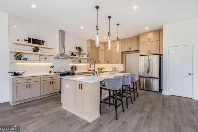 kitchen with a kitchen island with sink, stainless steel appliances, wall chimney range hood, open shelves, and a sink