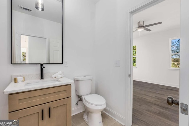 half bath with toilet, a ceiling fan, vanity, visible vents, and baseboards