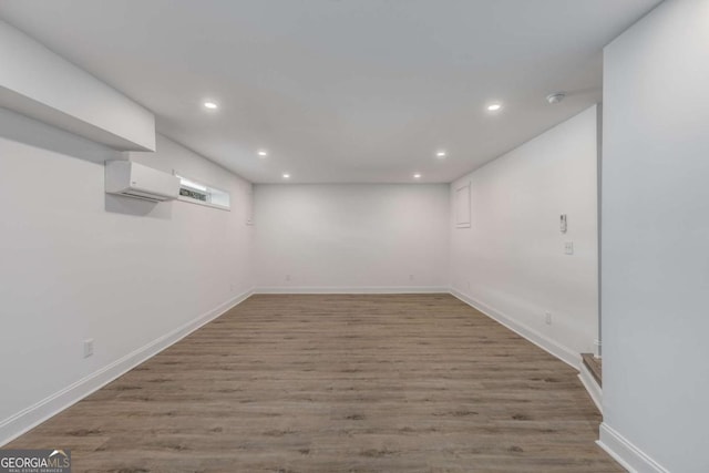 basement with recessed lighting, a wall unit AC, baseboards, and wood finished floors