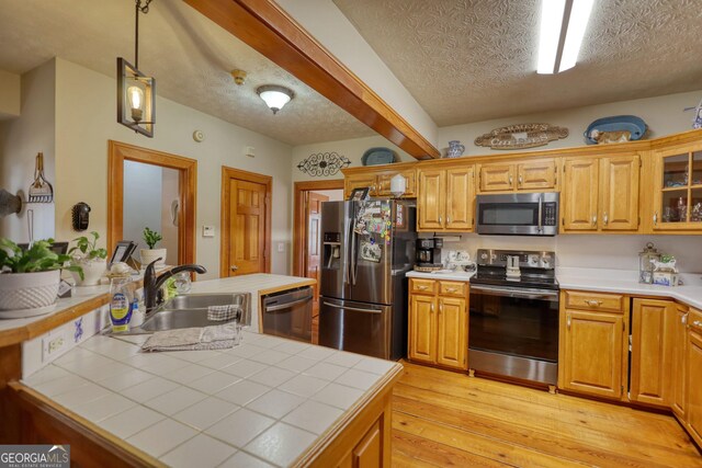 kitchen featuring stainless steel appliances, tile countertops, light wood finished floors, and a textured ceiling