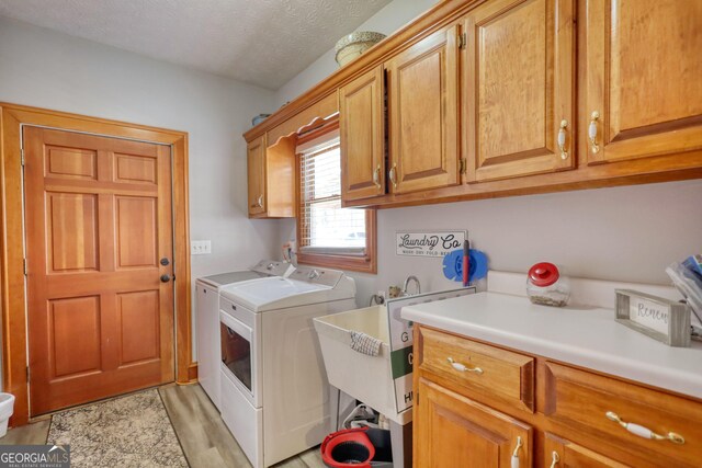 laundry area with light wood-style flooring, cabinet space, a textured ceiling, and separate washer and dryer