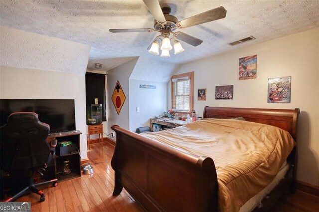 bedroom with a textured ceiling, a ceiling fan, visible vents, multiple closets, and light wood finished floors