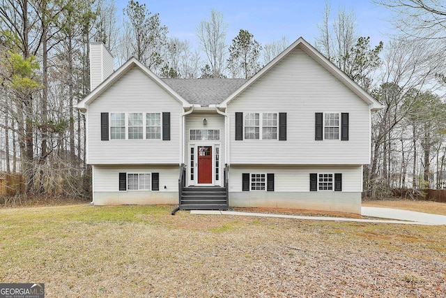 raised ranch featuring entry steps, a chimney, and a front yard