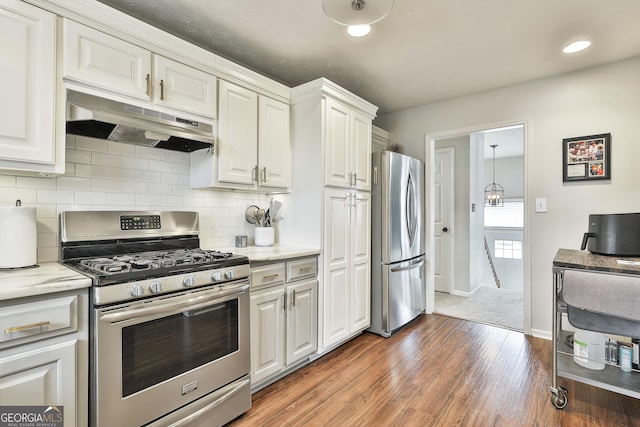 kitchen with under cabinet range hood, stainless steel appliances, wood finished floors, white cabinetry, and decorative backsplash