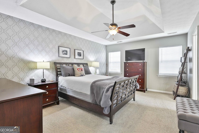 bedroom featuring baseboards, a tray ceiling, light colored carpet, and wallpapered walls