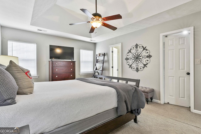 bedroom featuring light colored carpet, a ceiling fan, baseboards, visible vents, and a tray ceiling