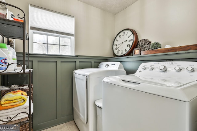 clothes washing area with a textured ceiling, a decorative wall, laundry area, wainscoting, and washing machine and clothes dryer