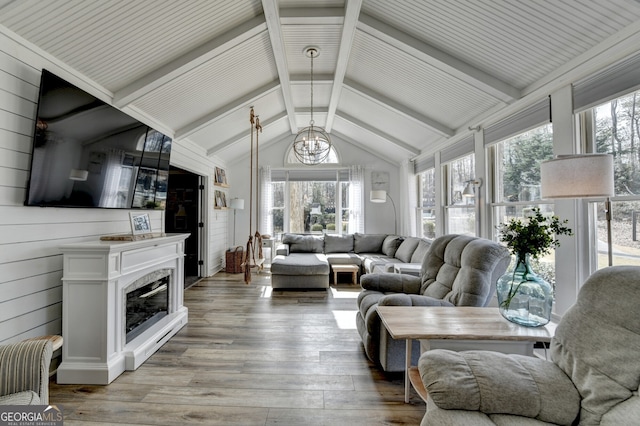 living room featuring a notable chandelier, lofted ceiling with beams, light wood-style floors, a glass covered fireplace, and wooden walls