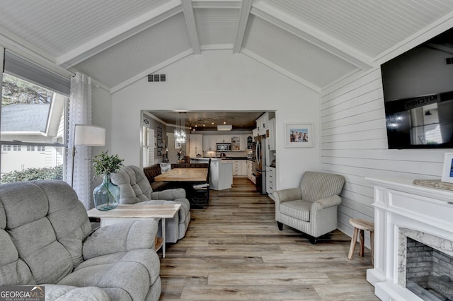 living room featuring beam ceiling, a fireplace, visible vents, light wood-style flooring, and high vaulted ceiling