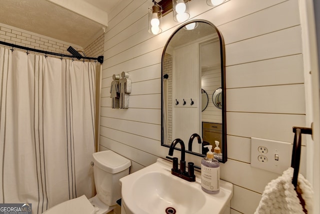 bathroom featuring curtained shower, wood walls, a sink, and toilet