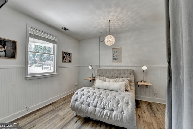 bedroom with visible vents, wood finished floors, and wainscoting