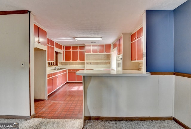 kitchen with light countertops, backsplash, a sink, oven, and a peninsula