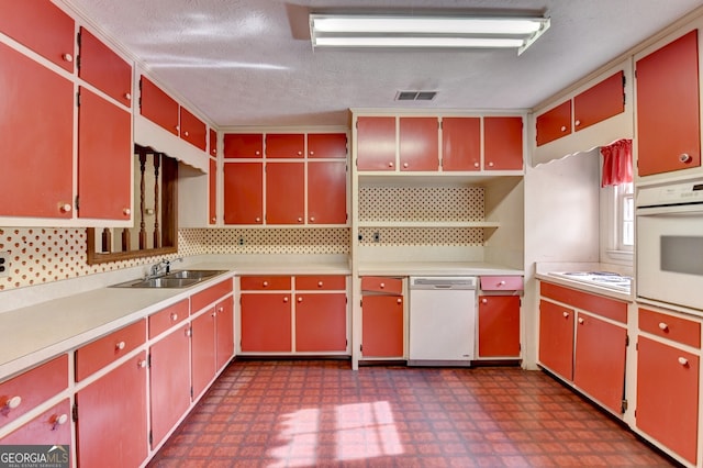 kitchen featuring dark floors, visible vents, red cabinetry, a sink, and white appliances