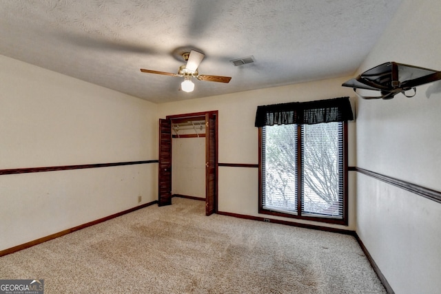 carpeted spare room featuring visible vents, baseboards, ceiling fan, and a textured ceiling