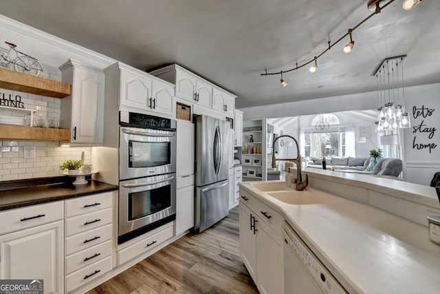 kitchen featuring decorative backsplash, open floor plan, wood finished floors, stainless steel appliances, and white cabinetry