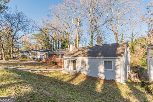 view of front of house featuring brick siding, a front lawn, a chimney, and a shingled roof